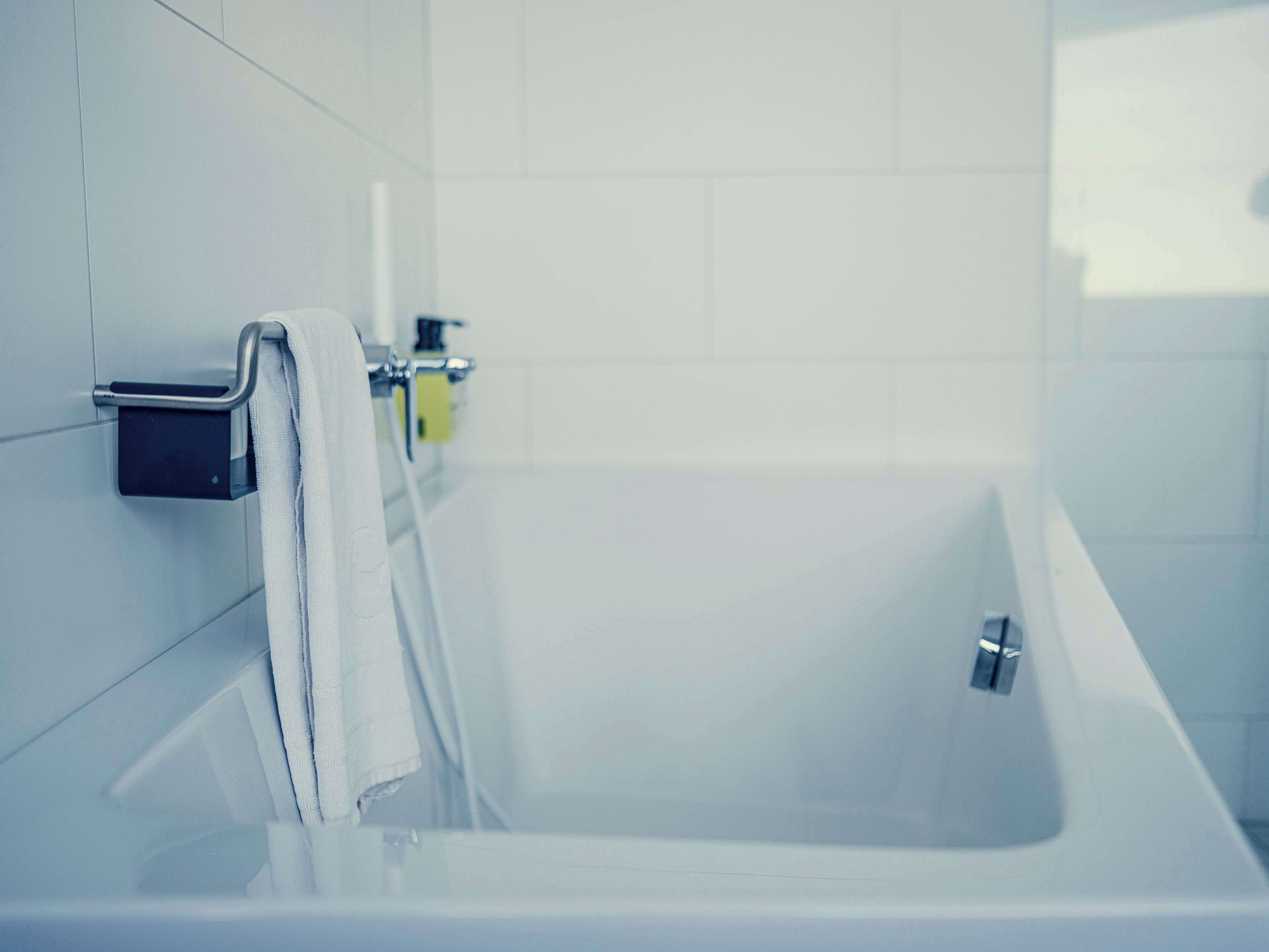 A modern bathroom with a bathtub, a towel rack, and a soap dispenser.