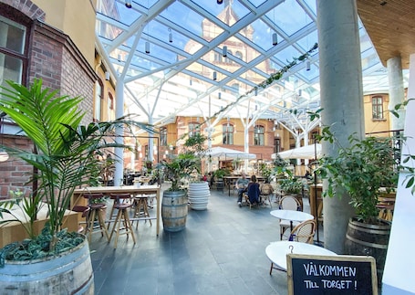 An indoor courtyard with tables and chairs, potted plants, and a sign that reads 'Welcome, please take your coat.'. U&Me, BW Signature Collection