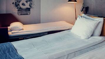 A single bed with a white mattress and pillow, a red chair, a black lamp, and a wall with a graphic.