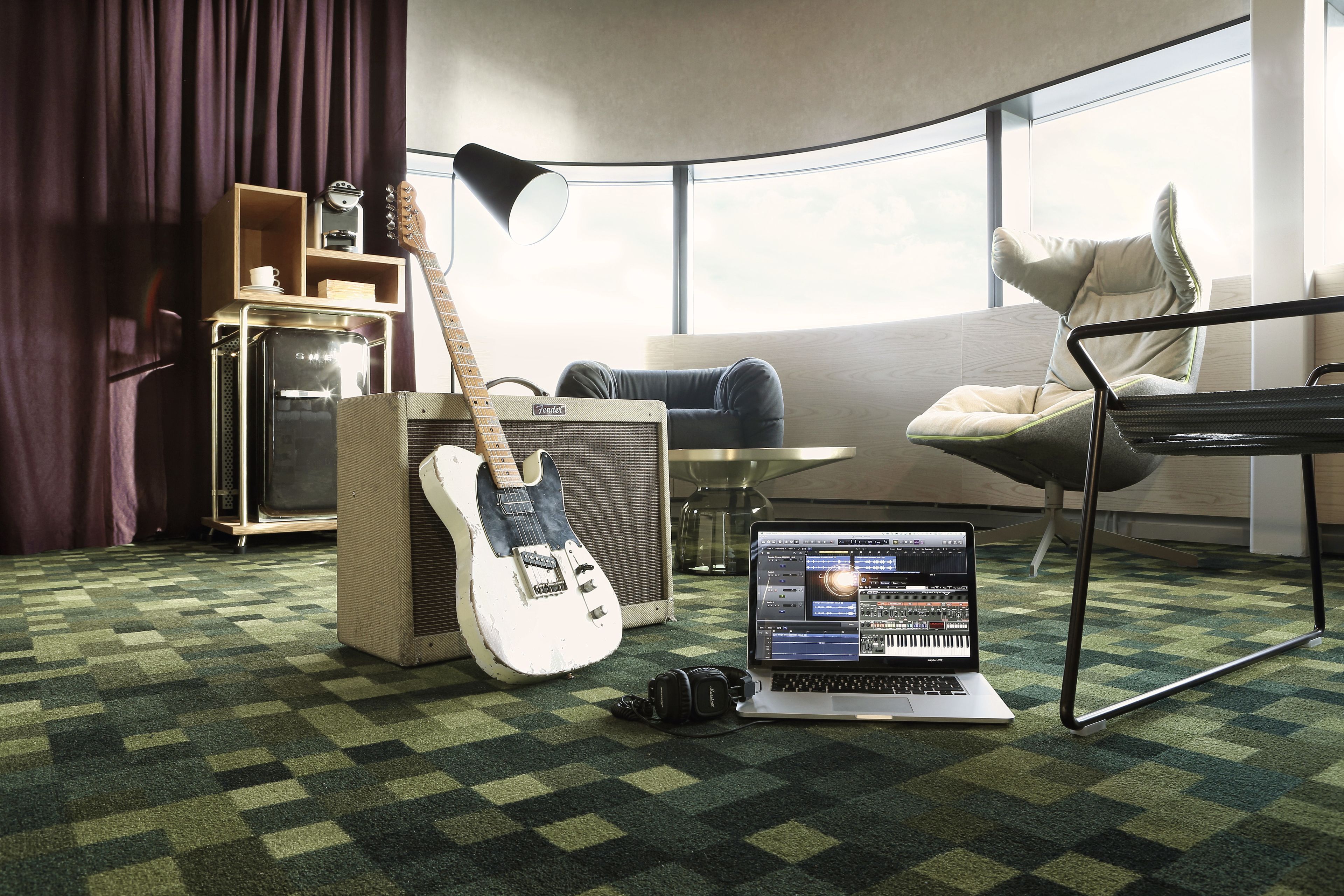 A room with a guitar, amplifier, laptop, and a chair.