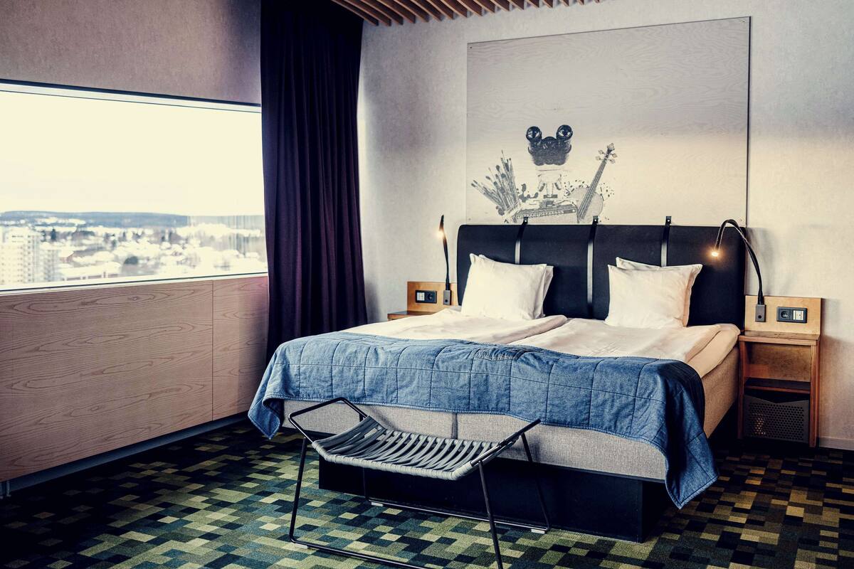 A modern hotel room with a large bed, a view of the city, and a unique ceiling design.