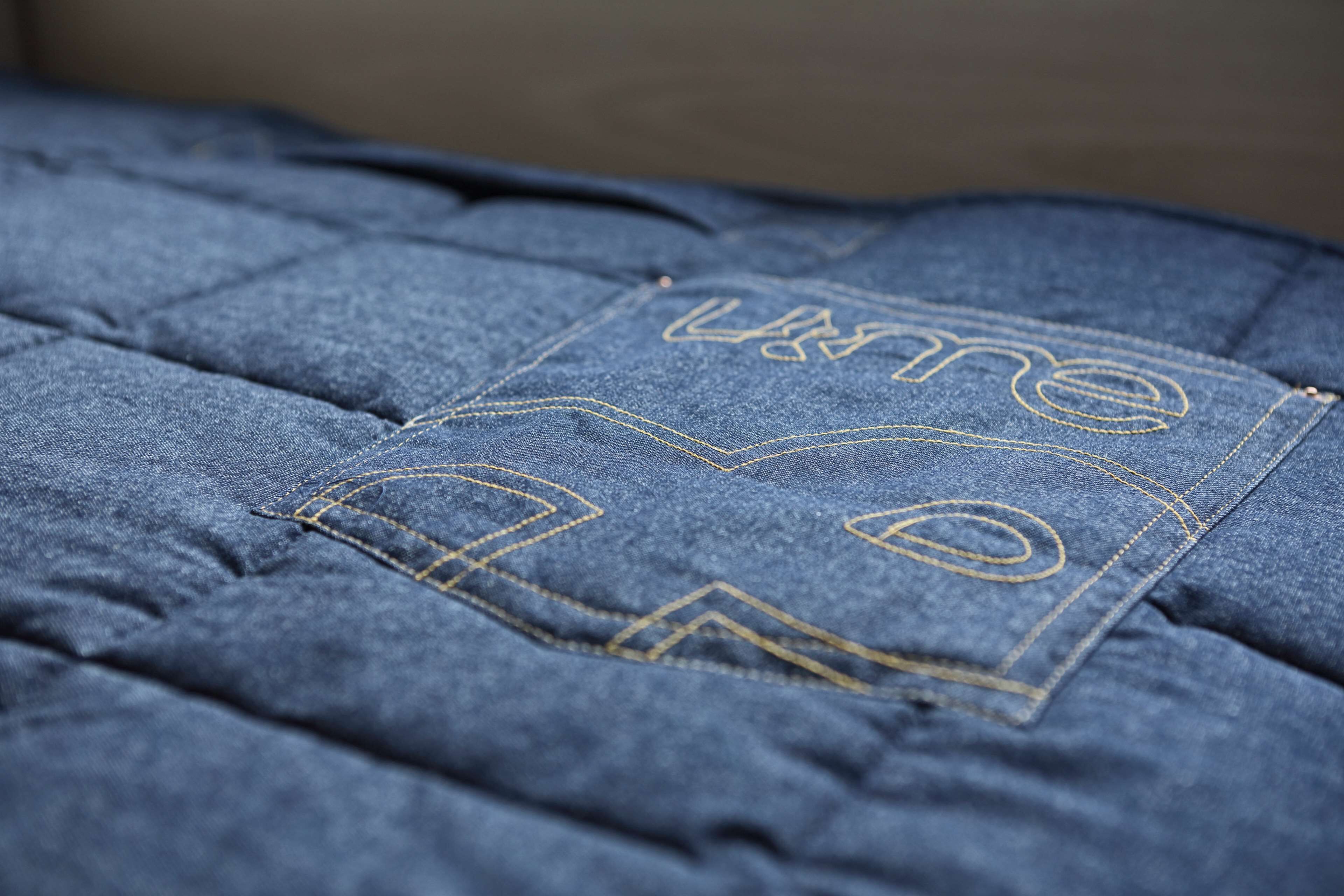 A close-up of a blue quilted fabric with a gold embroidered design.