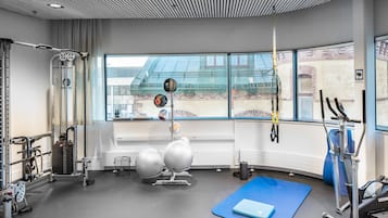 Un gimnasio con equipo de ejercicio, una colchoneta azul y una ventana con vistas a edificios.