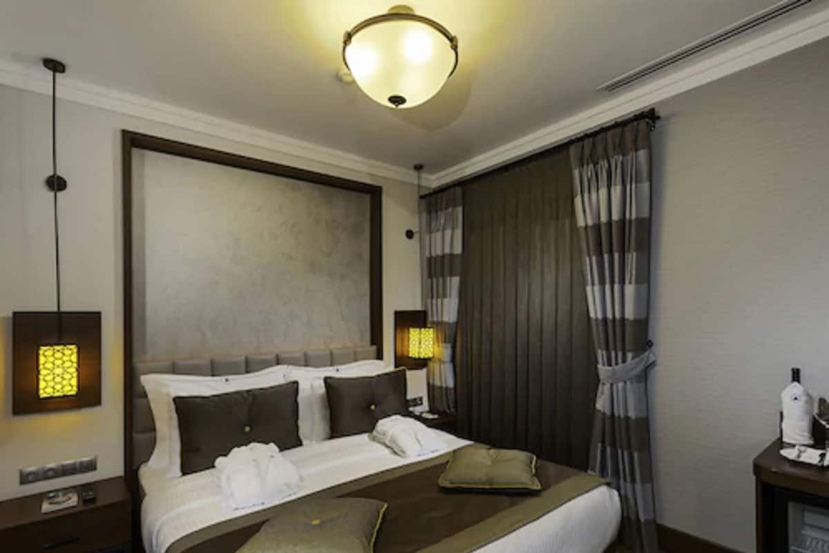 A hotel room with a large bed, two bedside tables, a nightstand, a lamp, and a curtain.