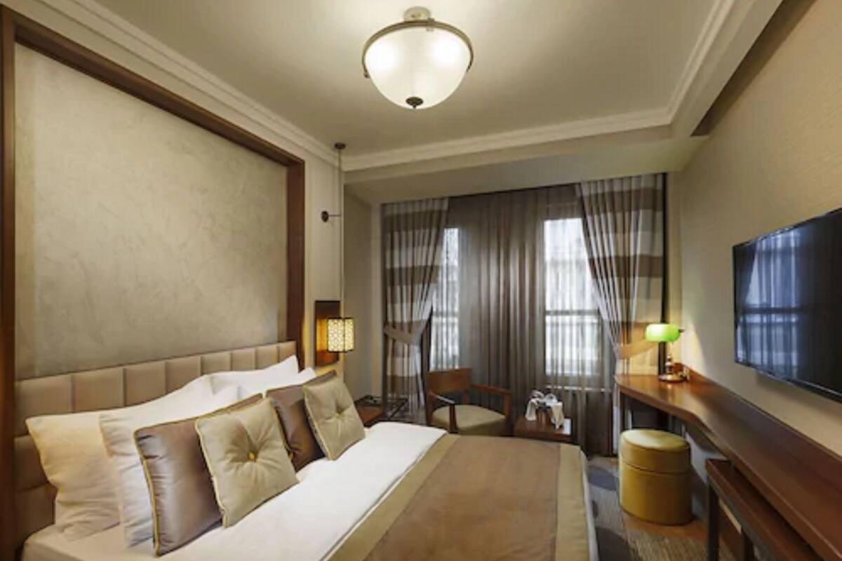 A hotel room with a large bed, a desk, a chair, a television, and a window with curtains.