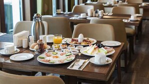 Un comedor de hotel con varias mesas dispuestas para el desayuno, incluyendo platos de comida, tazas y una cafetera.