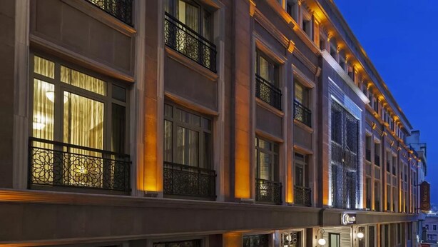 Un hotel de varios pisos con amplias ventanas y balcones, con iluminación cálida y fachada de piedra.