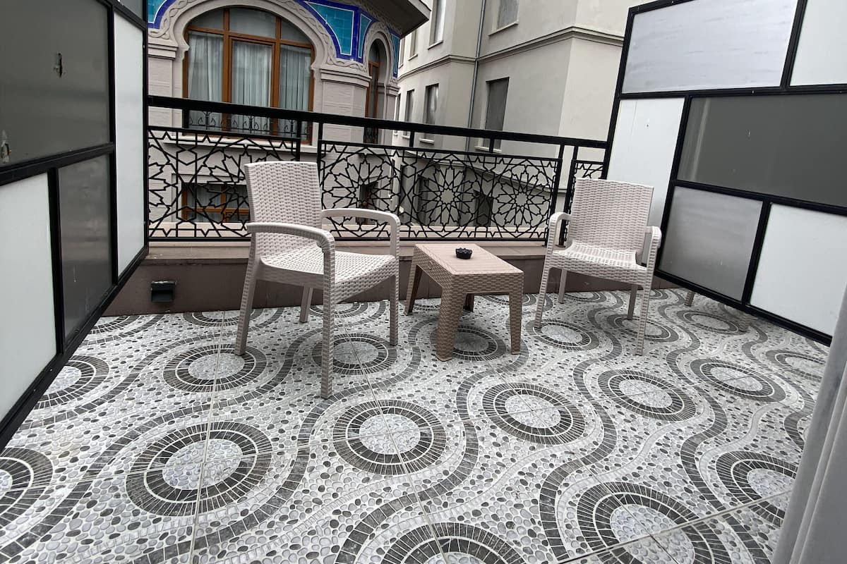 A balcony with patterned flooring, wicker furniture, and a view of adjacent buildings.