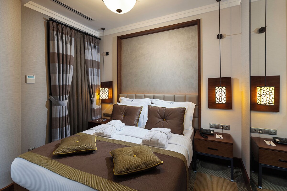 A hotel room with a large bed, a bedside table with a lamp, a nightstand, and a wall-mounted phone.