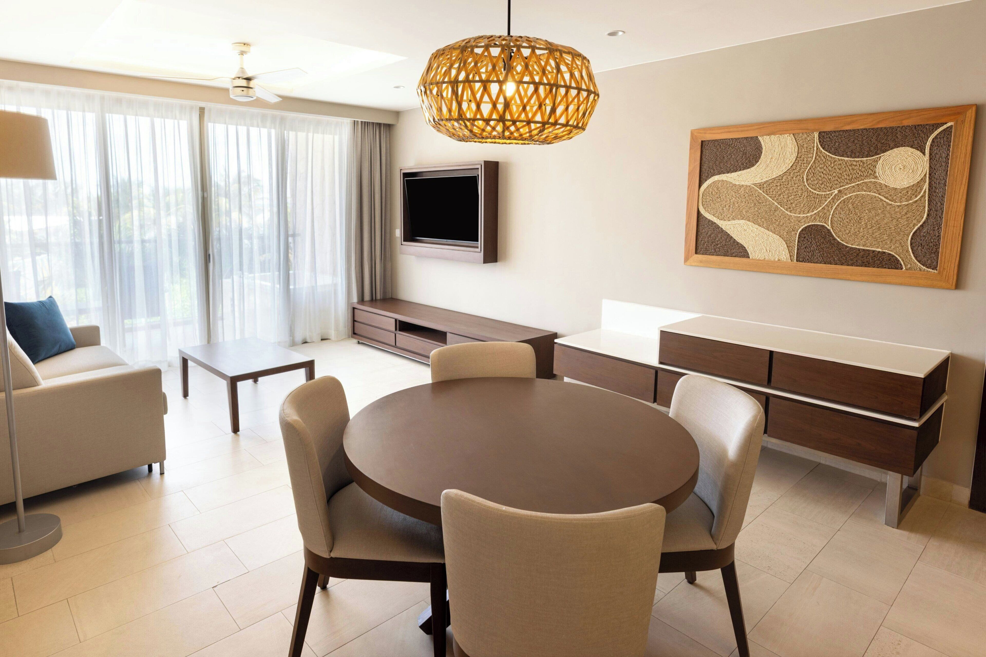 Una sala de estar moderna con una mesa de comedor redonda, sofás color beige y un televisor montado en la pared.