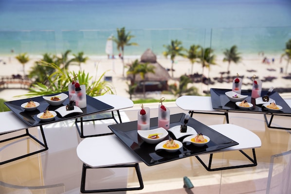 Un área de comedor frente a la playa, con mesas dispuestas para una comida, con vista al océano.