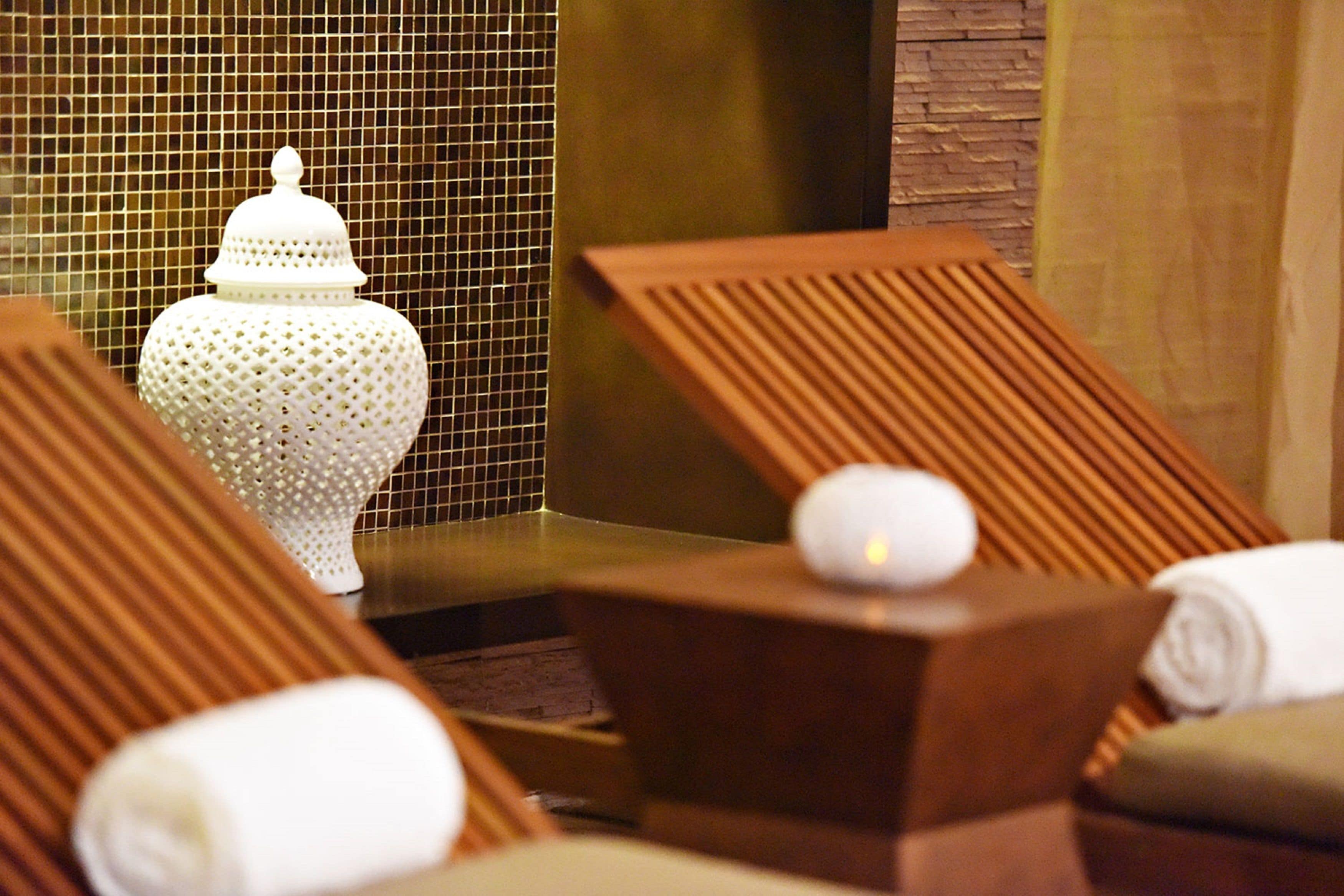 A spa area with wooden loungers, a white decorative urn, and a towel on a wooden stool.