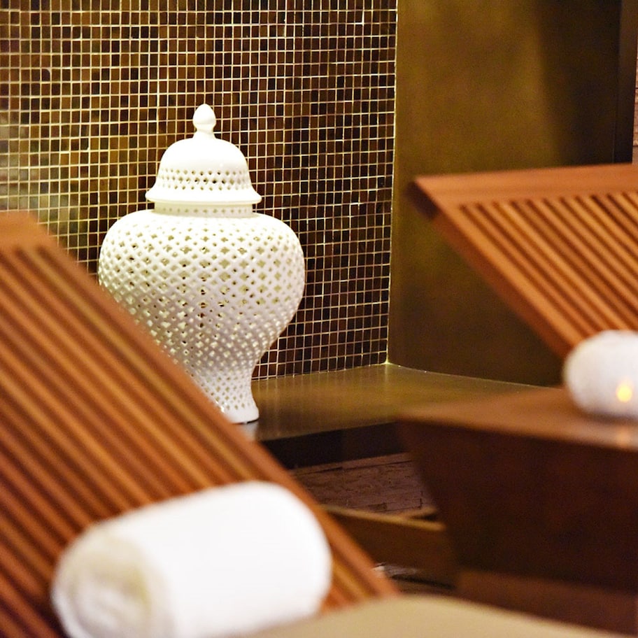 A spa area with wooden loungers, a white decorative urn, and a towel on a wooden stool.