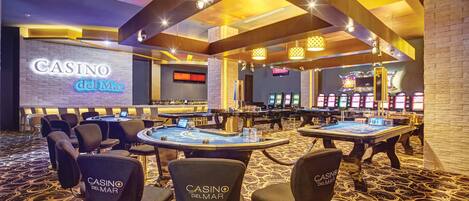 A casino interior with multiple blackjack tables, branded chairs, and slot machines.
