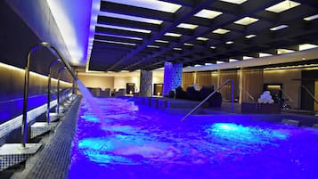 Una piscina interior moderna con un elemento acuático iluminado en azul, una zona de estar y un mostrador de recepción.