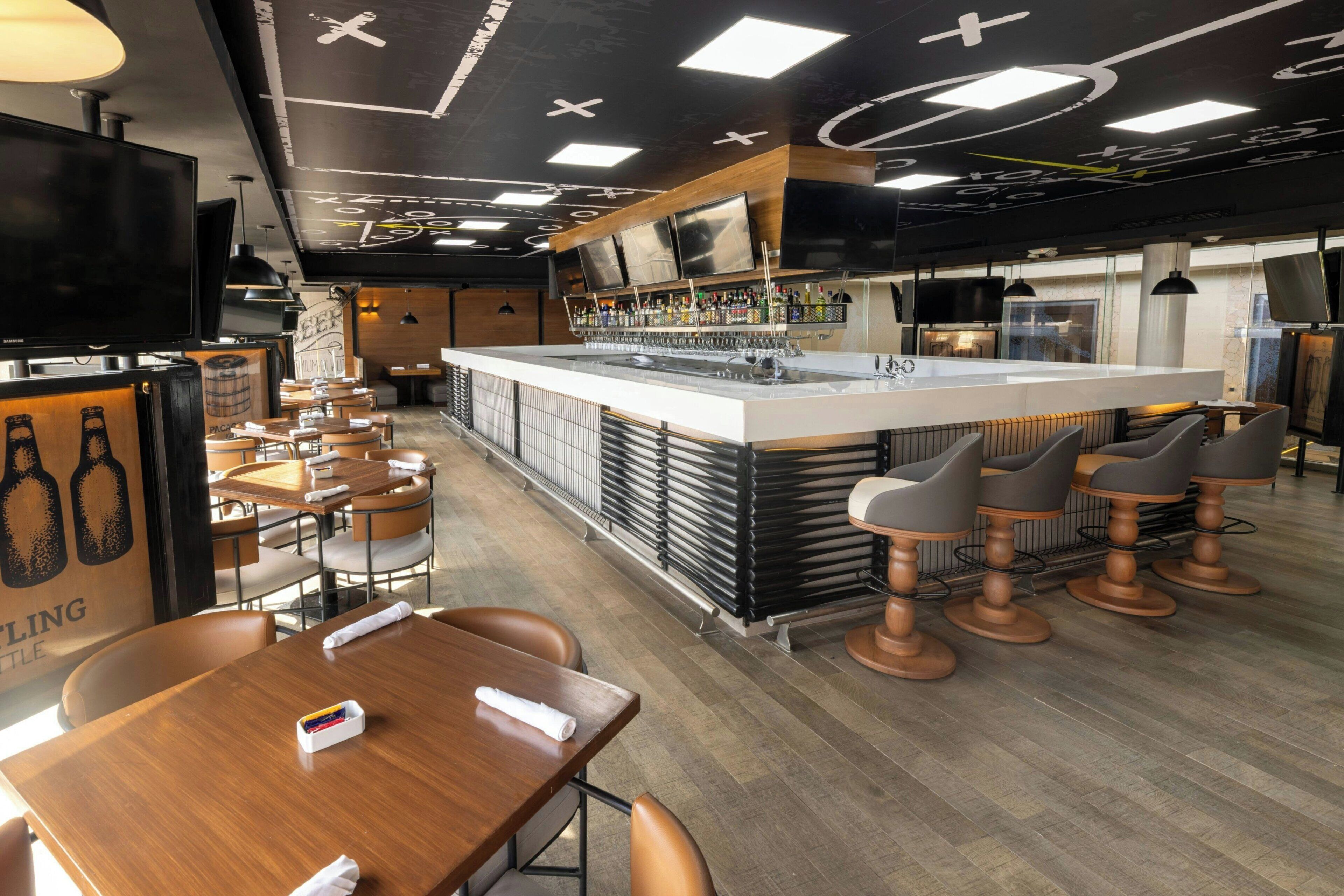 A modern bar area with a central island, bar stools, and a seating area with tables and chairs.