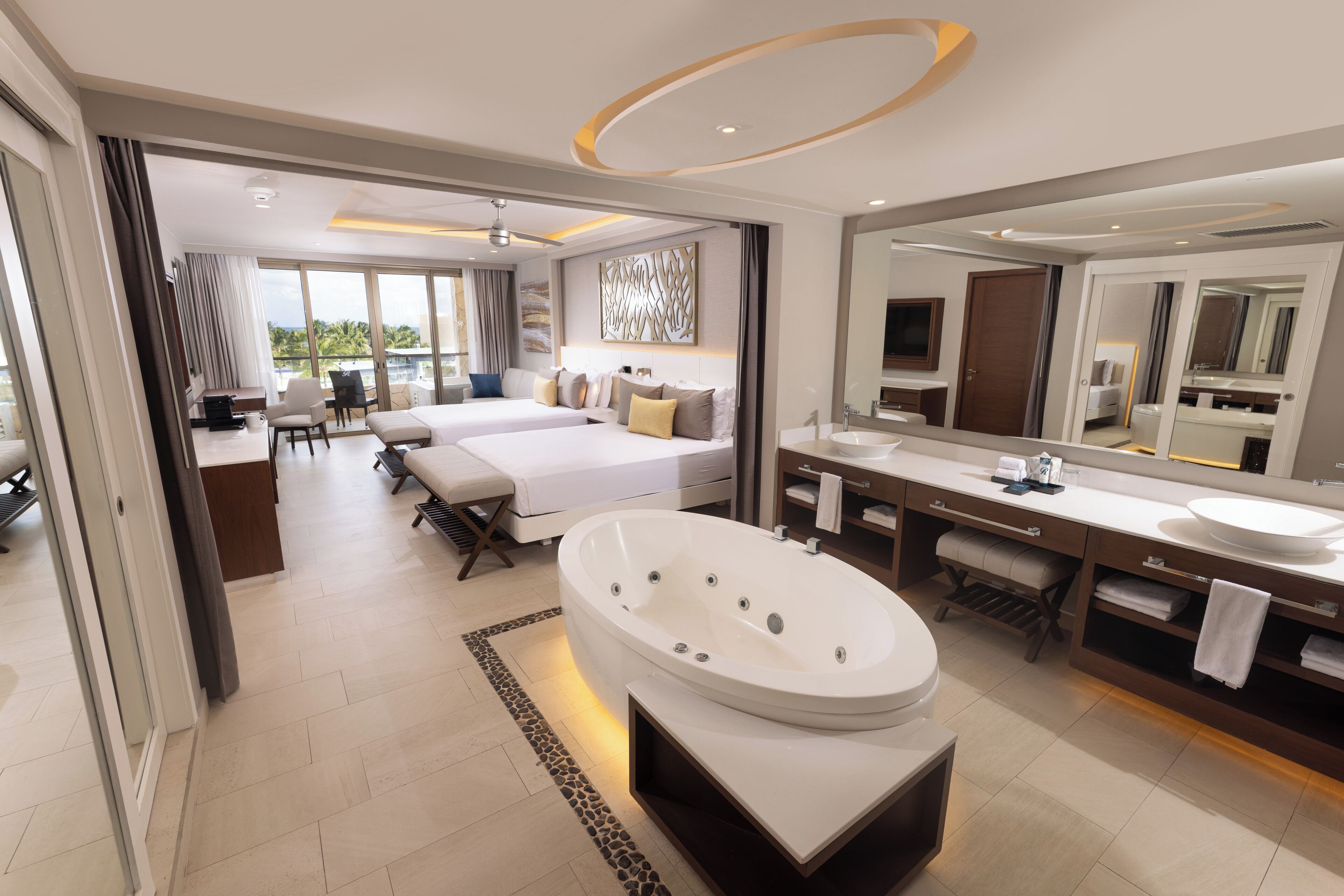 Una habitación de hotel moderna con una cama grande, un sofá independiente, un jacuzzi, un espejo amplio y vistas al exterior.