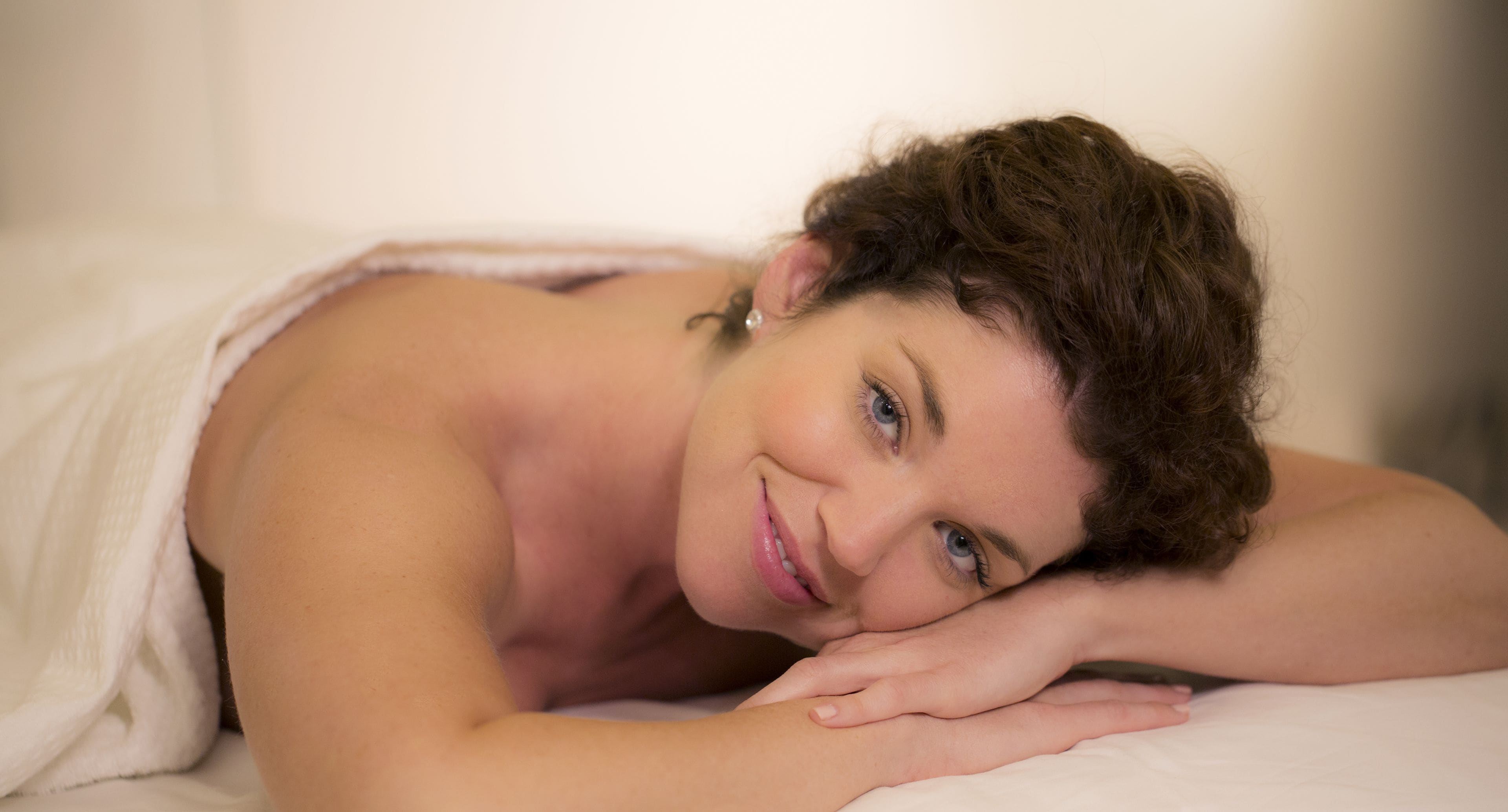 A person lying on a bed with a white sheet.