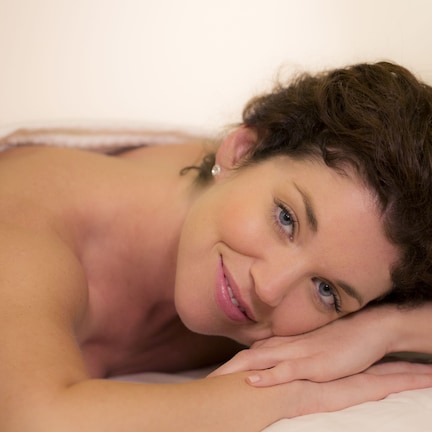 A person lying on a bed with a white sheet.