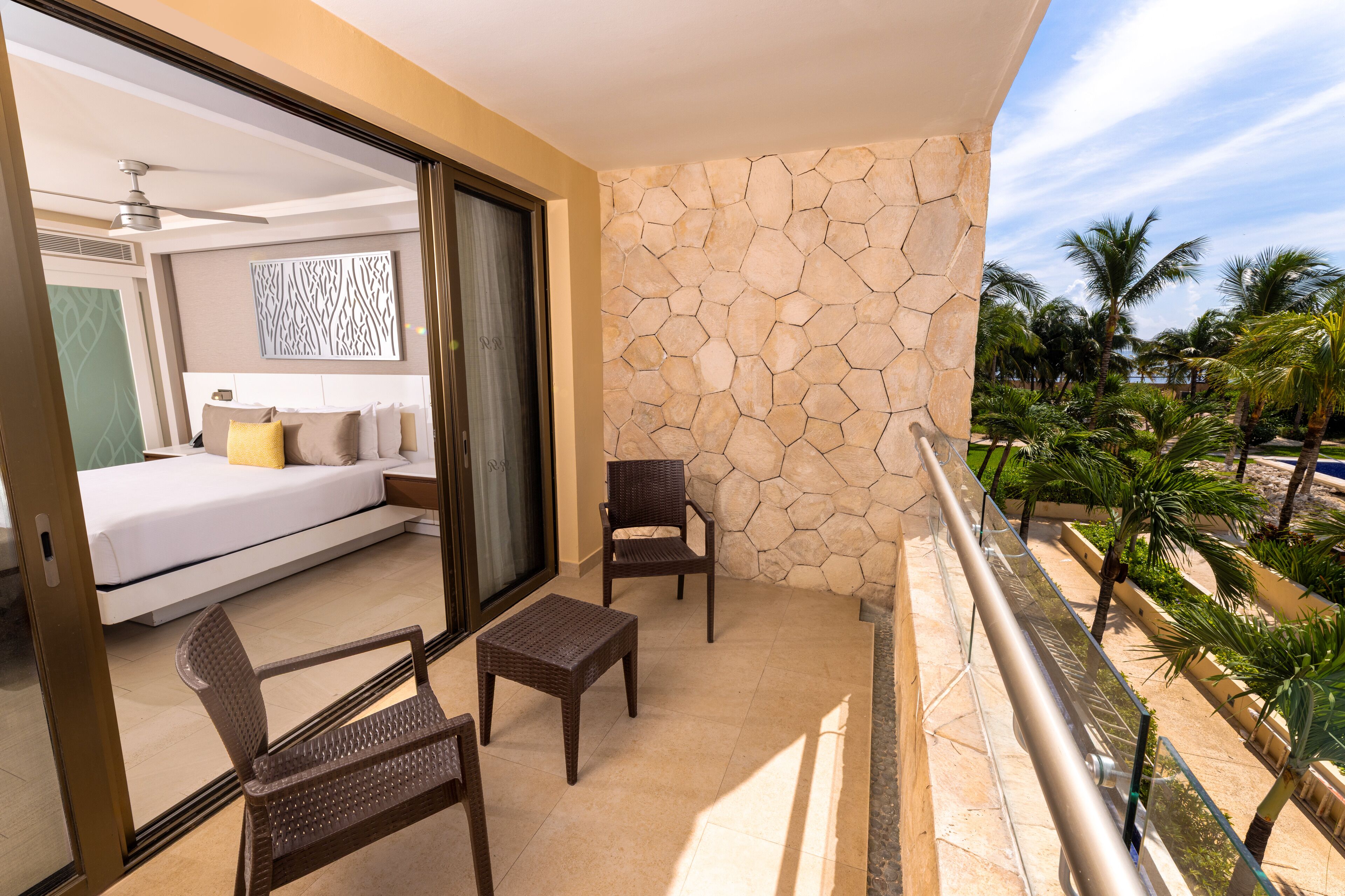 A balcony with a bed, two chairs, a small table, and a stone wall.