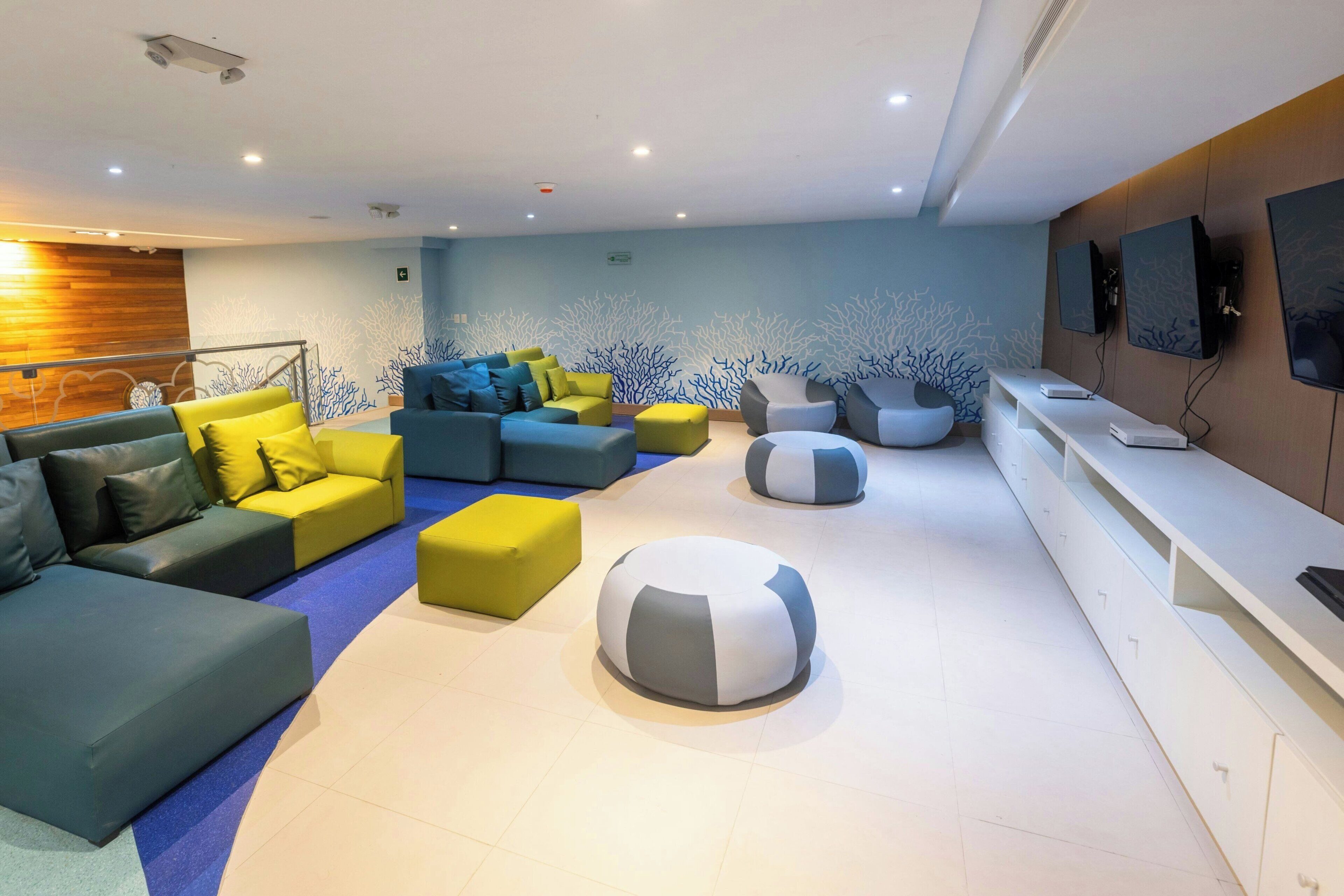 A modern lounge area with sofas and ottomans, a white reception desk, and a wall-mounted TV.