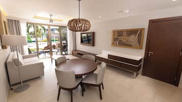 A modern hotel room with a dining area, a sofa, a TV, and a large wooden door.