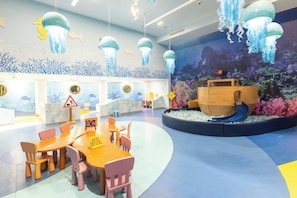 A children's play area with a slide, tables, chairs, and a mural of an underwater scene.