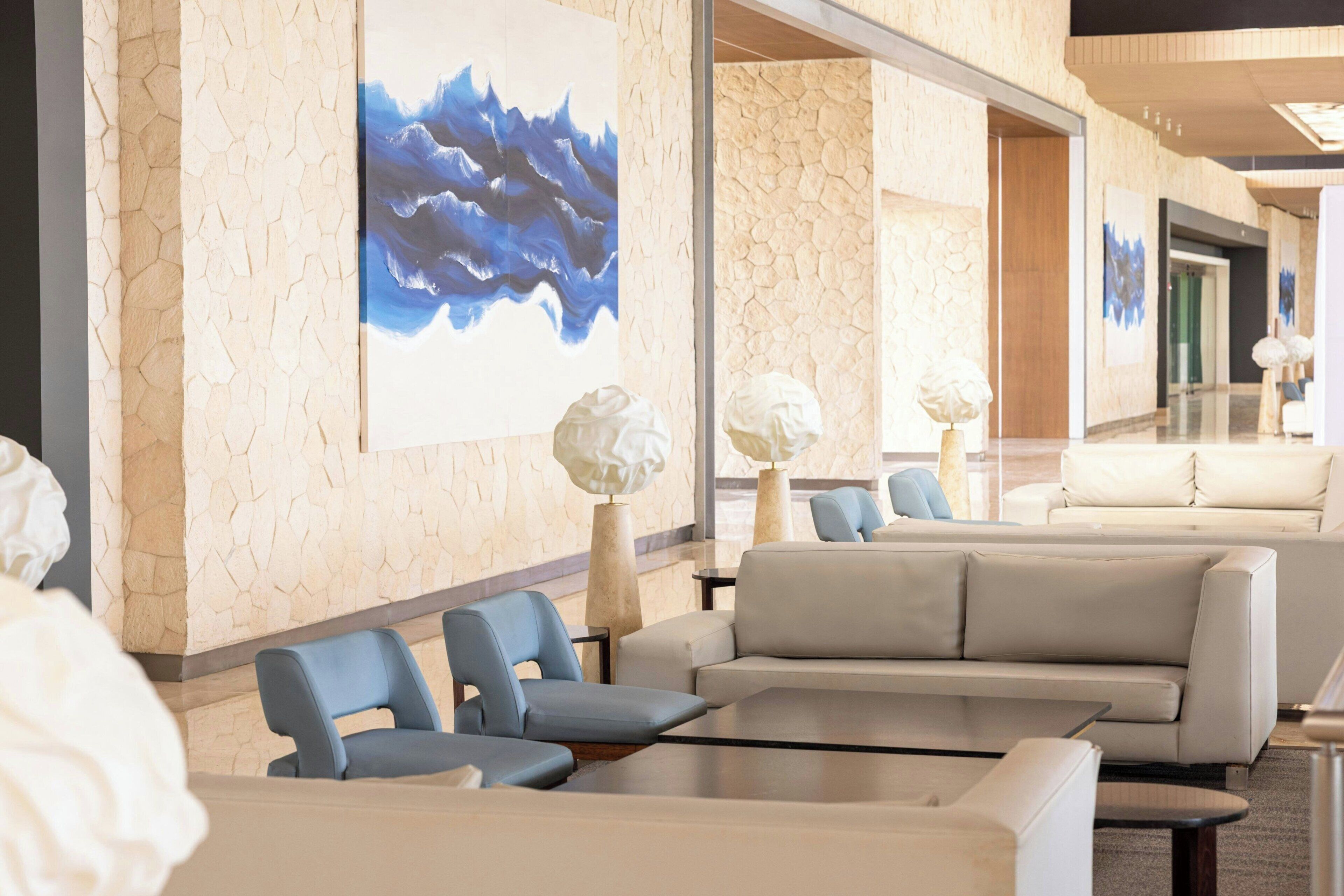 Vestíbulo de hotel con pared de piedra, un cuadro abstracto azul y arreglos de asientos modernos.