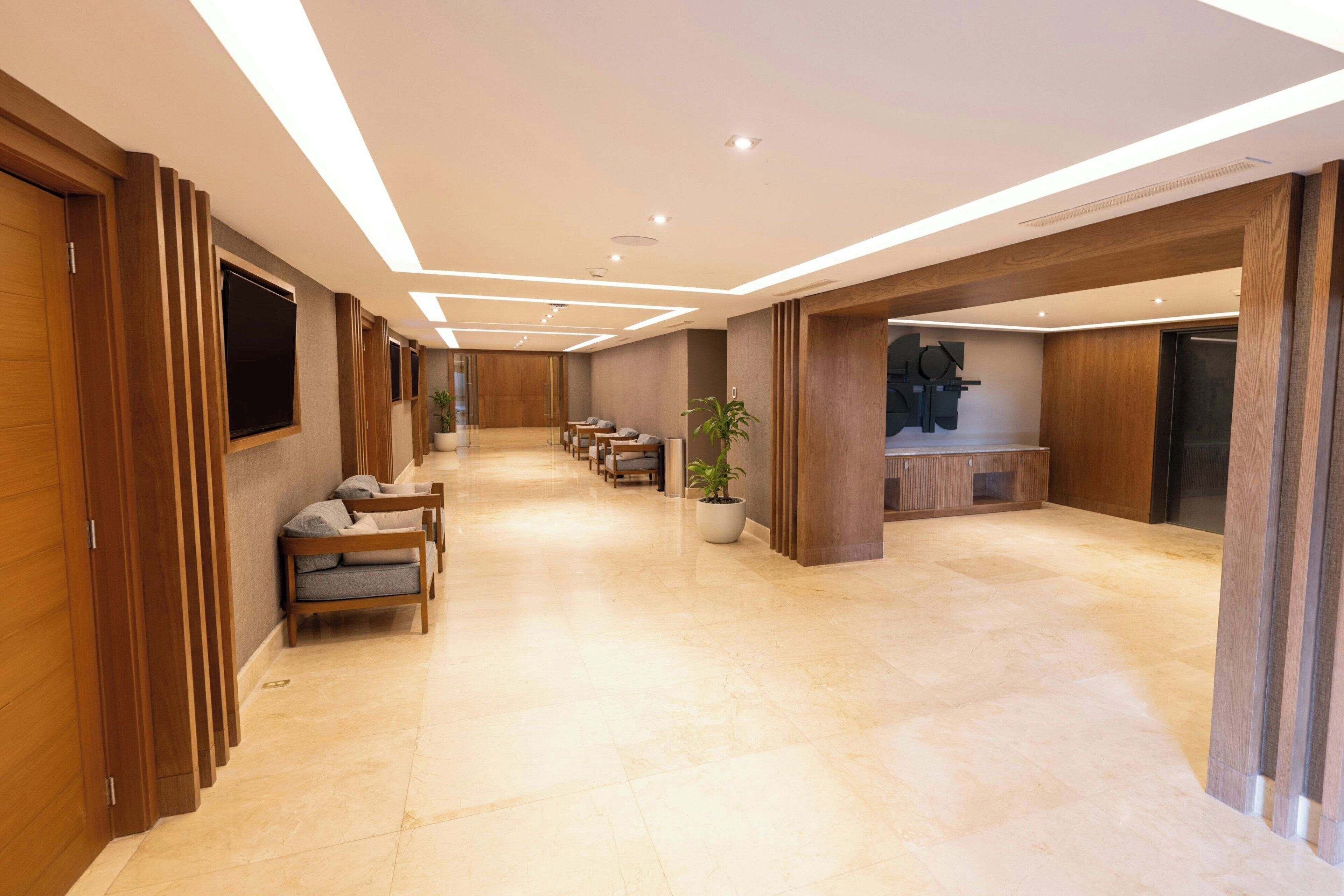 A hotel lobby with a long reception desk, seating area, and a large TV screen.