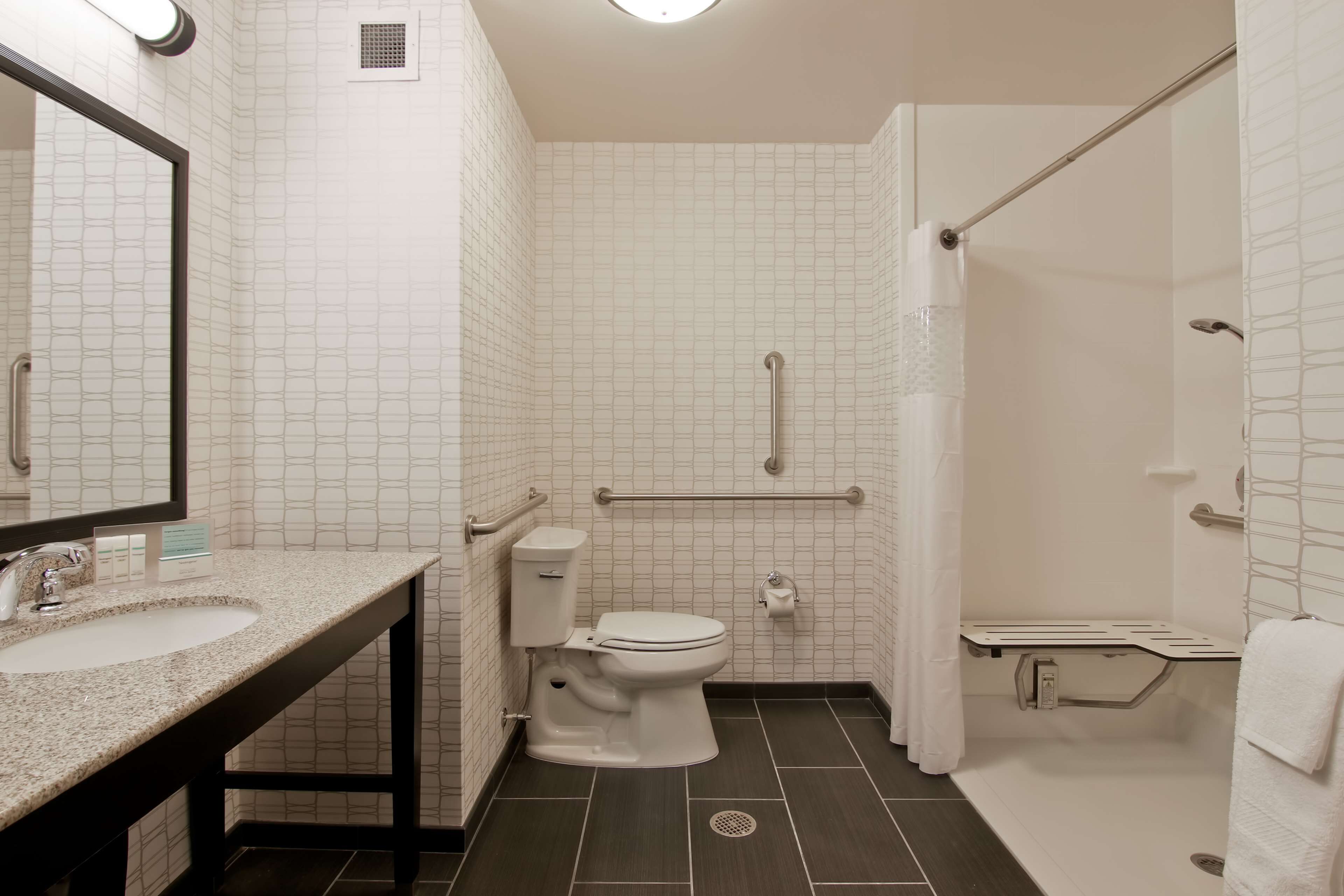 A bathroom with a sink, toilet, and shower. It has grab bars and a handrail.