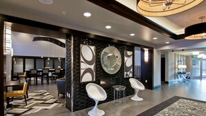 A modern hotel lobby with a seating area, a reception desk, and a decorative wall with abstract art. - Hampton Inn & Suites Bellevue Downtown-Seattle (Bellevue)