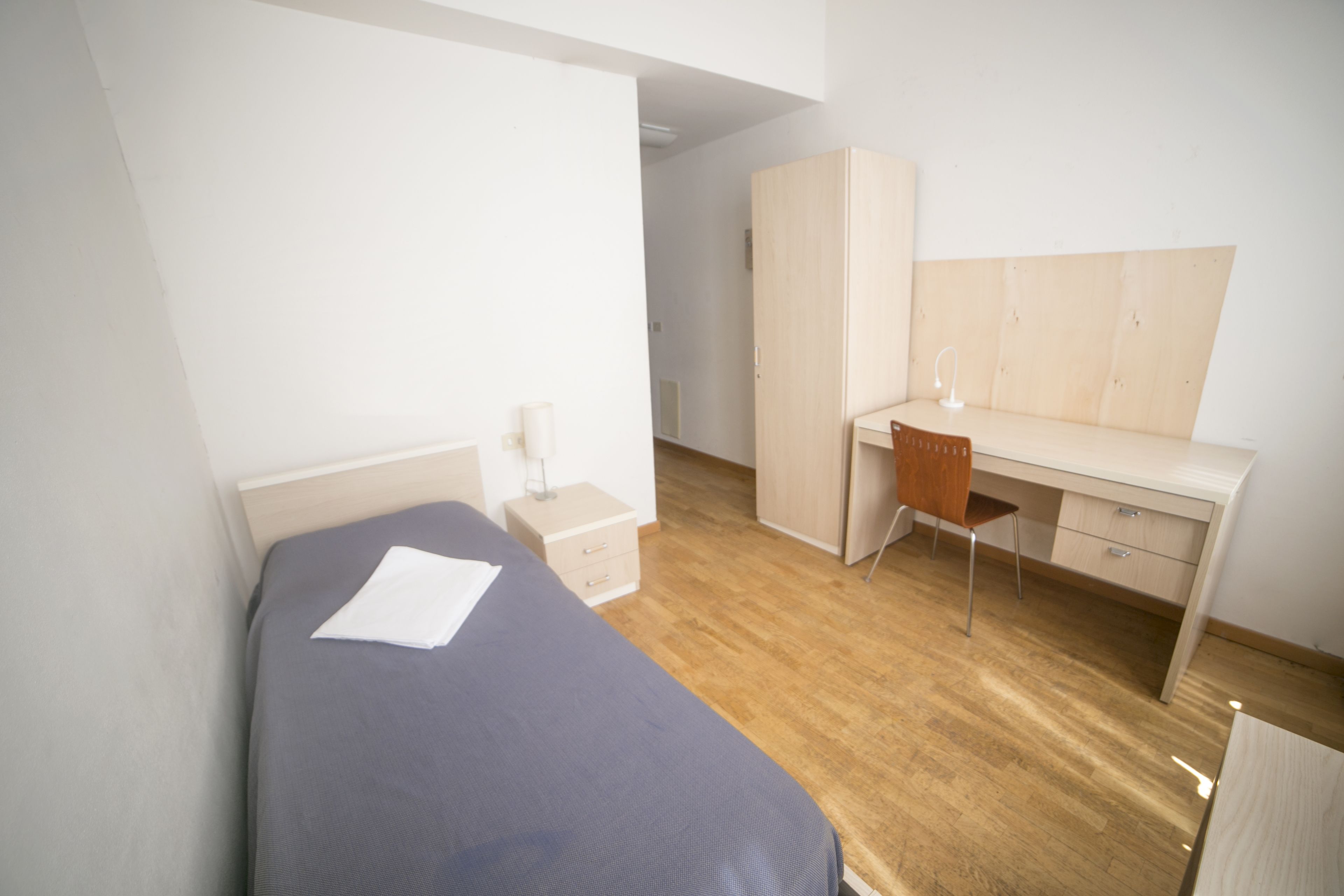 A bedroom with a bed, a desk, a chair, and a wardrobe.
