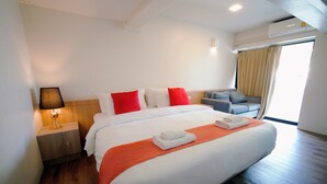 A hotel room with a large bed, a nightstand with a lamp, a sofa, and a window with curtains. -  Wild Orchid Villa Bangkok (Bangkok)