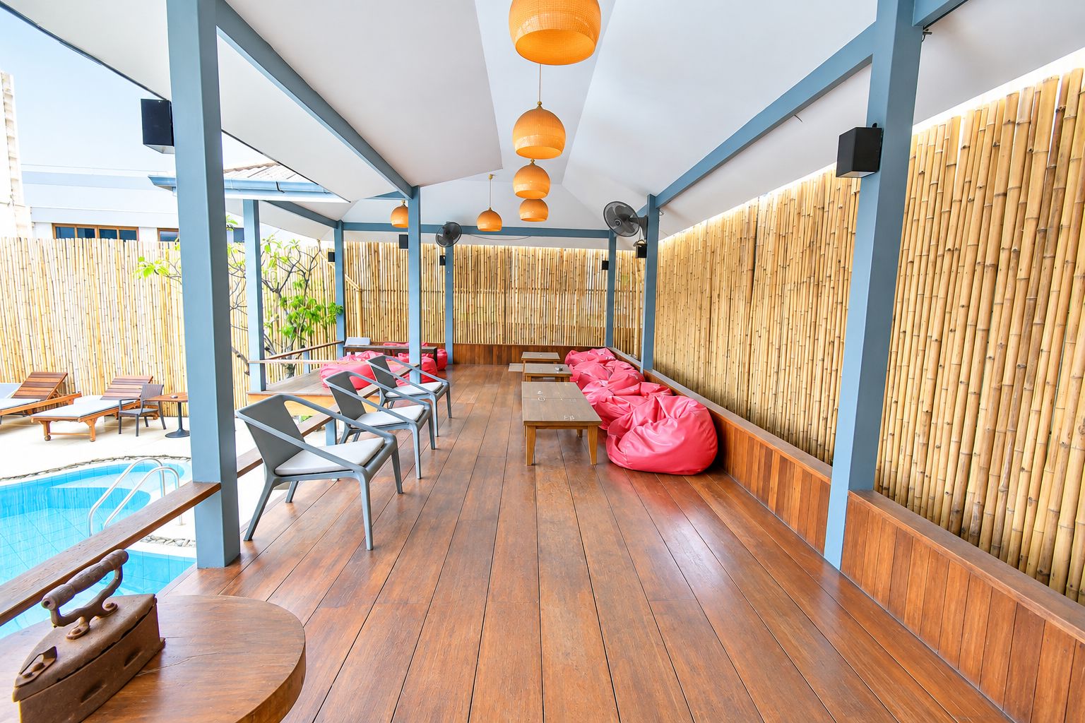 Un área junto a la piscina con suelo de madera, sillones de descanso y pared de bambú.