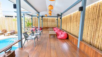 A poolside area with wooden flooring, lounge chairs, and a bamboo wall.