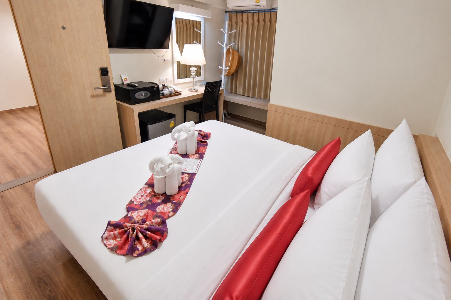A hotel room with a neatly made bed, a desk with a computer and a lamp, and a television mounted on the wall.