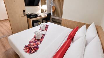 A hotel room with a neatly made bed, a desk with a computer and a lamp, and a television mounted on the wall.