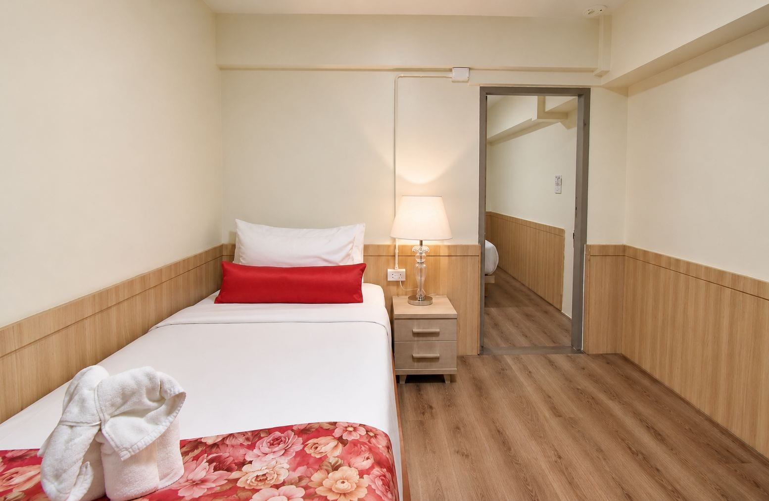 A hotel room with a bed, a nightstand, a lamp, a mirror, and a door leading to another room.