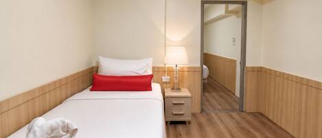 A hotel room with a bed, a nightstand, a lamp, a mirror, and a door leading to another room.