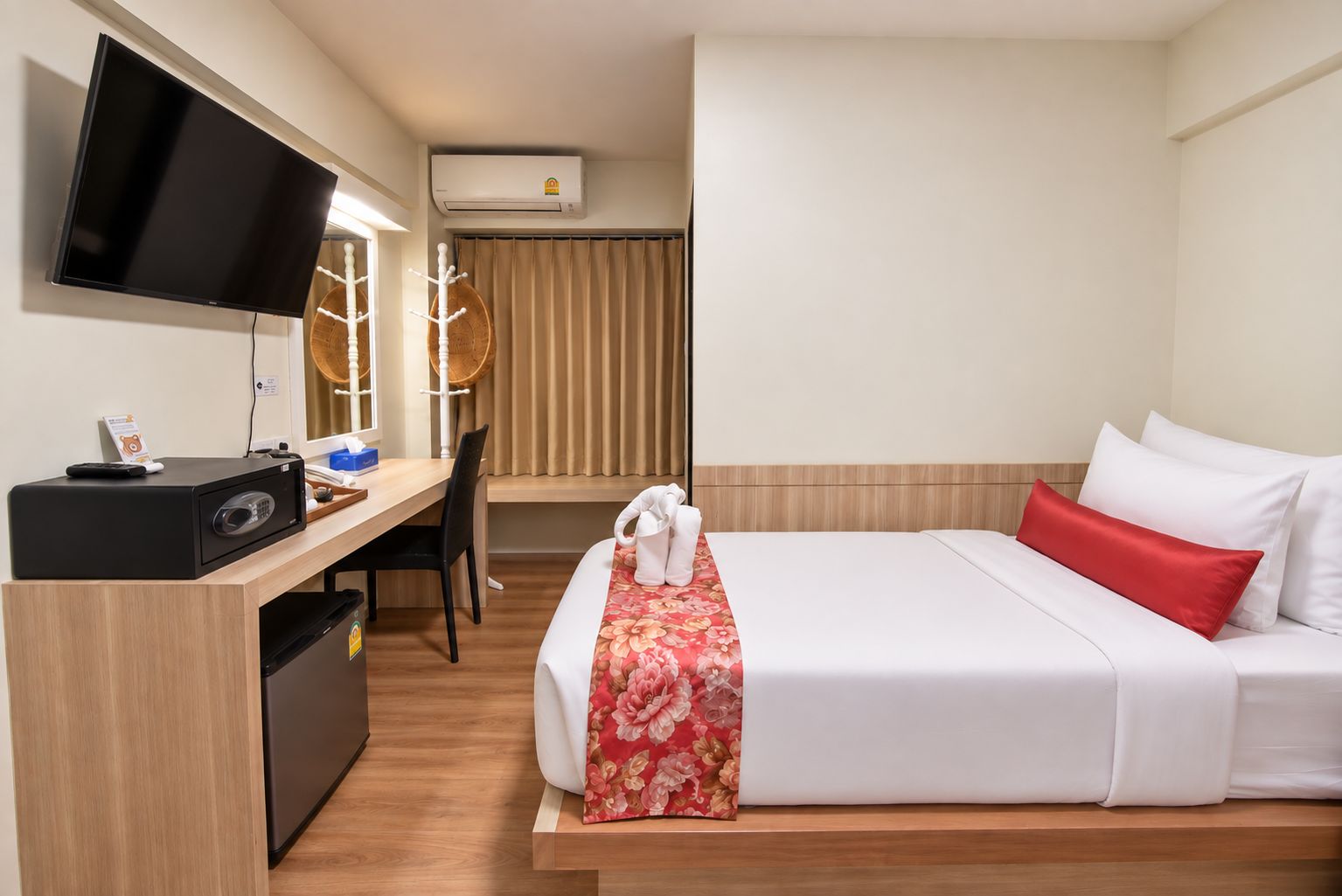 A hotel room with a bed, a desk, a TV, and an air conditioning unit.