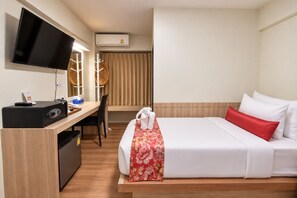 A hotel room with a bed, a desk, a TV, and an air conditioning unit. -  Wild Orchid Villa Bangkok (Bangkok)
