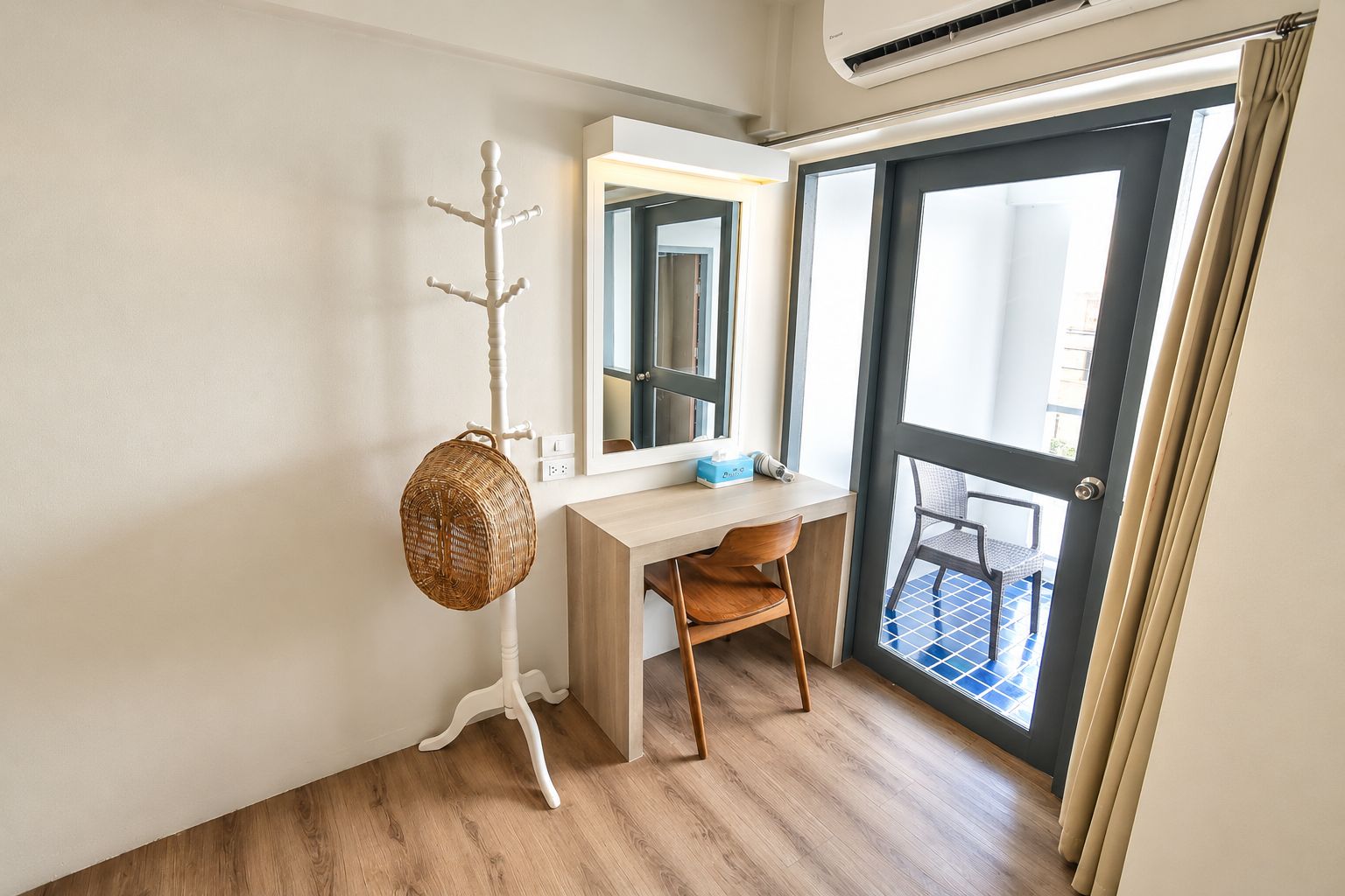A room with a desk, chair, and a coat rack with a basket.