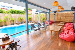 A poolside area with wooden flooring, lounge chairs, and red bean bags.