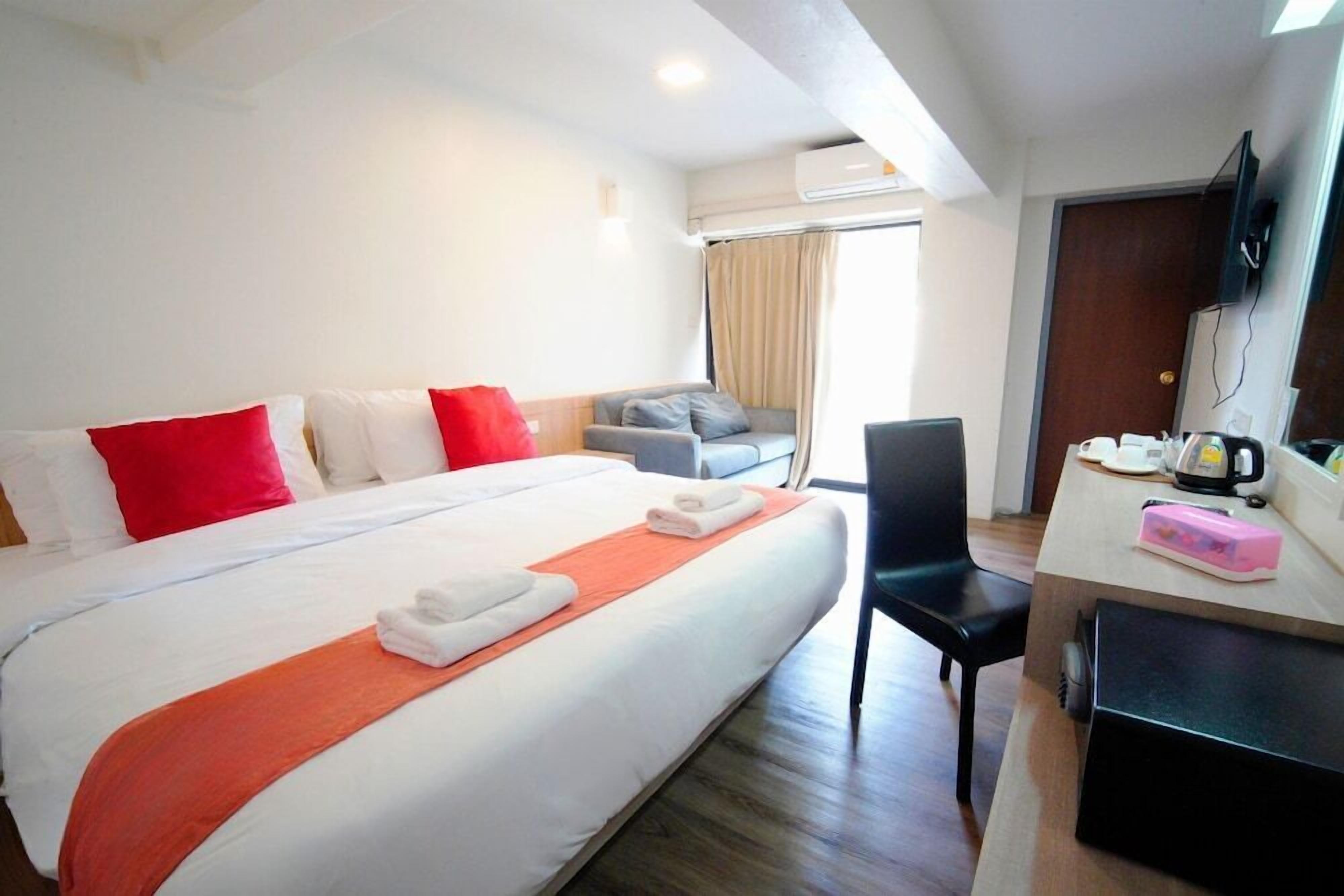 A hotel room with a bed, a desk with a chair, a television, and a window with curtains.