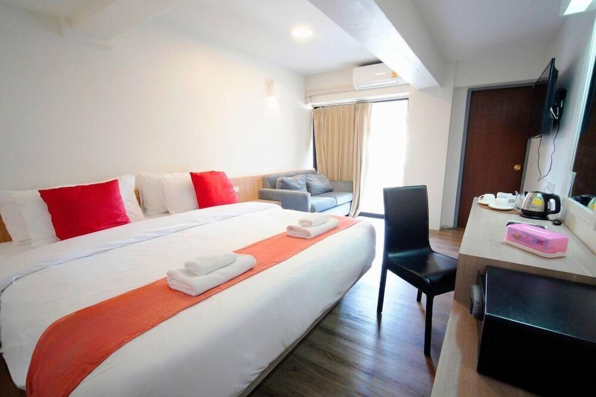 A hotel room with a bed, a desk with a chair, a television, and a window with curtains.