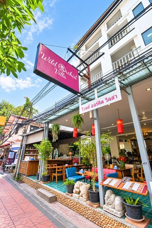 A building with a sign for 'Wild Orchid Villa' and a covered outdoor seating area with tables and chairs. -  Wild Orchid Villa Bangkok (Bangkok)