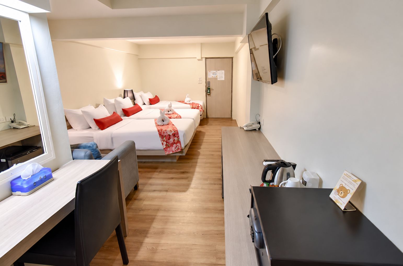 A hotel room with a bed, bedside table, chair, desk, and a TV mounted on the wall.