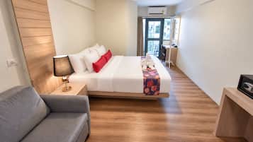 A hotel room with a bed, a bedside table with a lamp, a sofa, and a wooden floor.