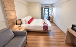 A hotel room with a bed, a bedside table with a lamp, a sofa, and a wooden floor. -  Wild Orchid Villa Bangkok (Bangkok)