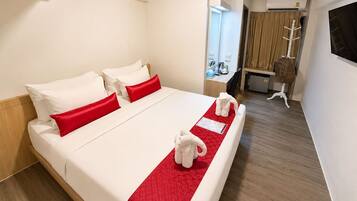 A hotel room with a bed, a desk, a chair, an air conditioning unit, and a television.